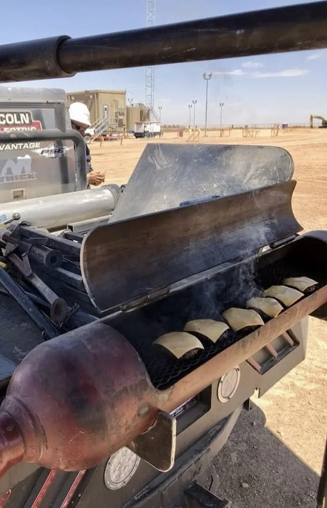 Homemade welding rig truck grill fabricated from a steel cylinder cooking food on an oilfield jobsite